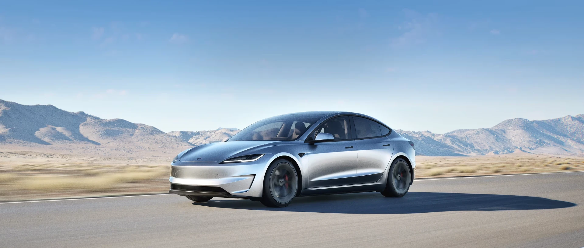 Silver Tesla Model 3 driving through a desert highway
